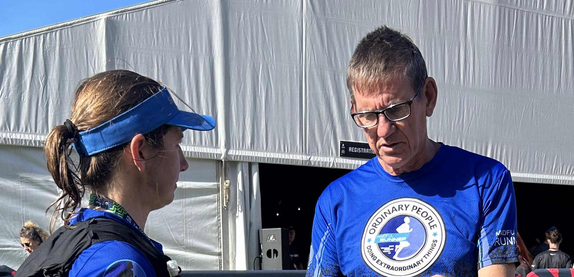 A coach talks an athlete through her kit and plan at the side of a race, the athlete listening in running vest and visor.